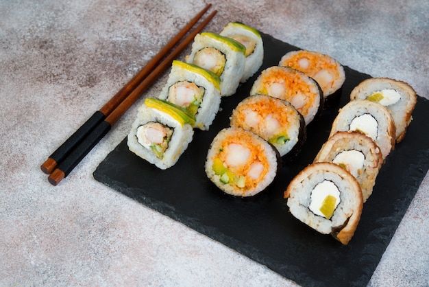 Set of sushi rolls with vegetables, cream cheese and shrimp. Traditional Japanese food on a concrete background.