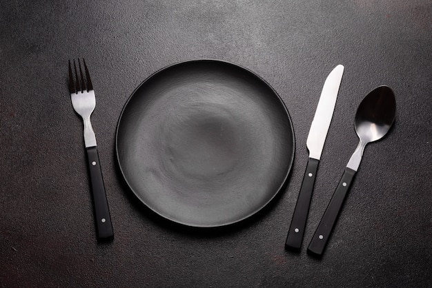 Set of tableware ready for the meal with black copy space. Metal knife, fork, spoon and plate