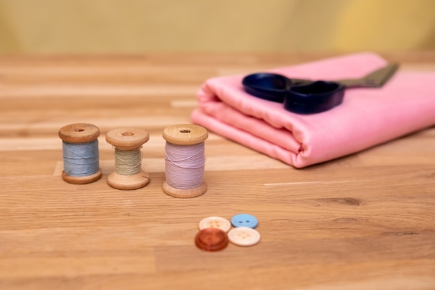 Set of tailoring accessories. Close up of a stack of folded pink fabric, sewing scissors, and spools of thread