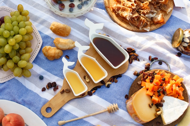 Set of three white sauceboats with sweet honey on wooden tray at picnic food lay out