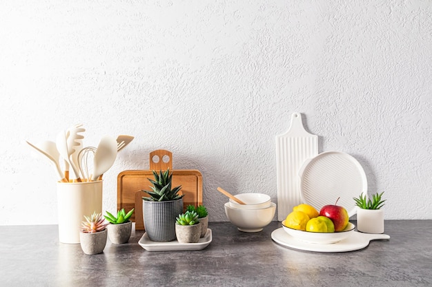 A set of various dishes tools a bowl of fruit on a stone countertop opposite a gray textured wall space for text still life