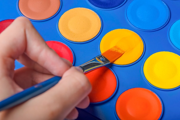 A set of watercolor paints and a brush for drawing closeup childs hand with a paintbrush selective f