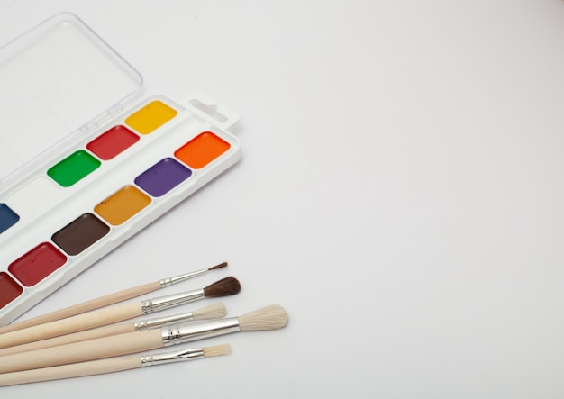 A set of watercolor paints and paint brushes on a white background with a copy space for text. Close-up