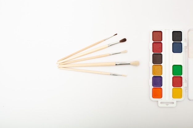 A set of watercolor paints and paint brushes on a white background with a copy space for text. Close-up