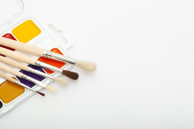 A set of watercolor paints and paint brushes on a white background with a copy space for text. Close-up