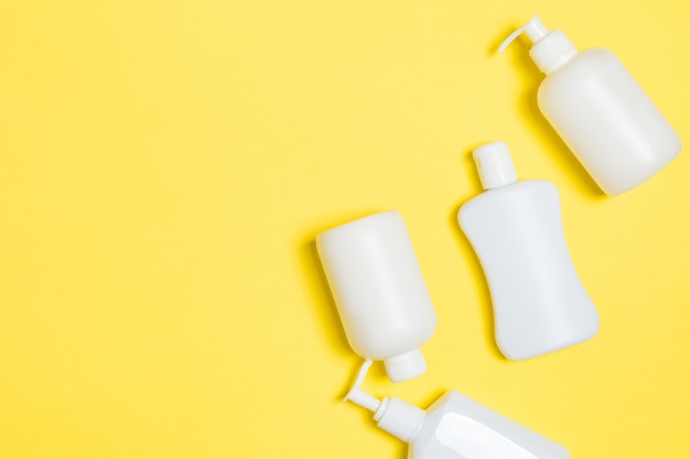 Set of White Cosmetic containers isolated on yellow background, top view with copy space. Group of plastic bodycare bottle containers