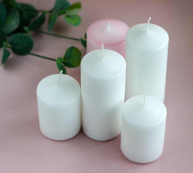 Set of white and pink wax candles with green leaves on the pink background