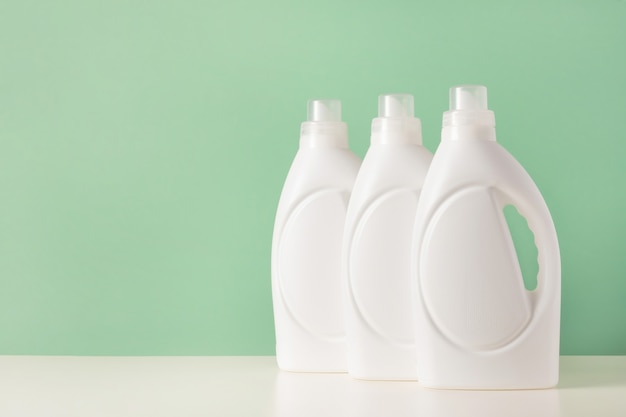 Set of white plastic bottles of liquid laundry detergent or cleaning agent or bleach or fabric softener. Blank mockup packaging for bio washing product on green background. Laundry day