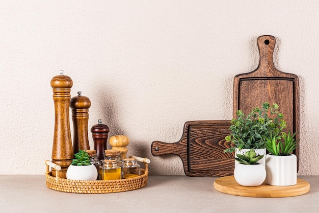 Set of wooden spice mills and glass jars with spices on a round wicker tray on a stone countertop in the interior of a modern kitchen space