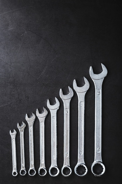 A set of wrenches on a textured black background in a row. Top view, free space