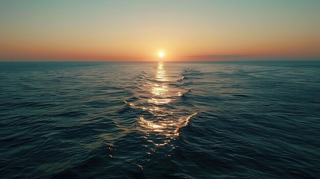 The setting sun casts a golden path across the dark blue sea The waves are small and gentle and the sky is clear The scene is peaceful and serene