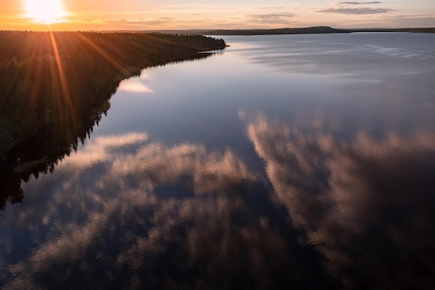 Setting sun above lake coastline and lake surface reflecting colorful clouds Karelia Russia