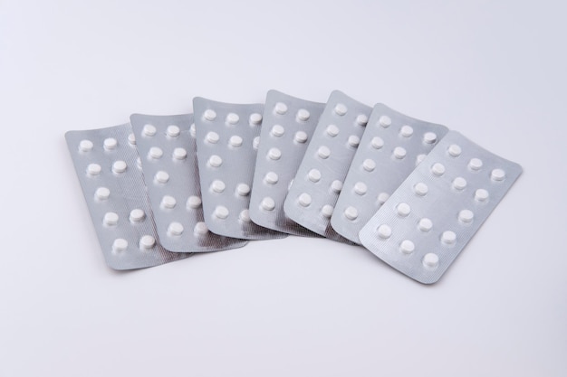 Seven medical blisters with pills lie isolated on a white-gray background, evenly spread out in the shape of a fan.