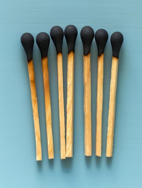 Photo seven unlit wooden matches with black heads in a neat row on light blue background minimalist and