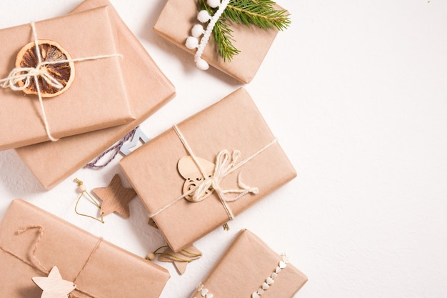 Several Christmas gift boxes in eco friendly style on a white background, decor from wooden Christmas tree toys, dried orange and spruce branch