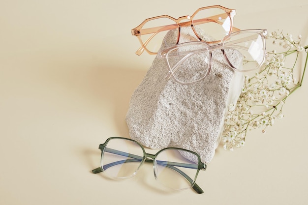 Several different trebdy eye glasses with fashion frames and concrete podium on beige background