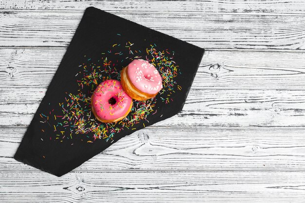 Several fresh donuts in a black ceramic plate on a wooden table with copy space