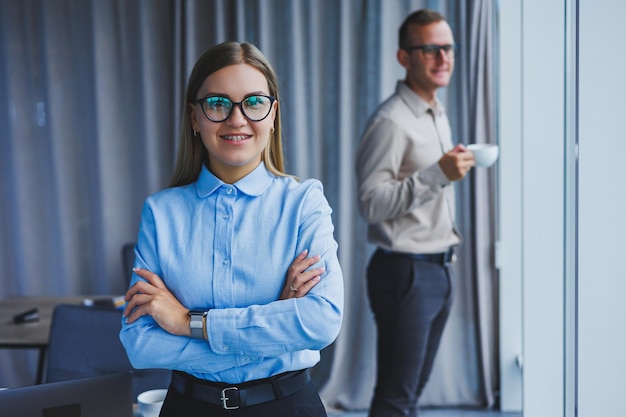 Several friendly colleagues are standing by the office window A business woman in glasses stands on the background of a man in a shirt Selective focus Portrait of business people