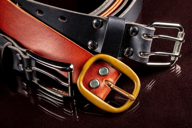 Several leather belts with a metal buckle on a dark background