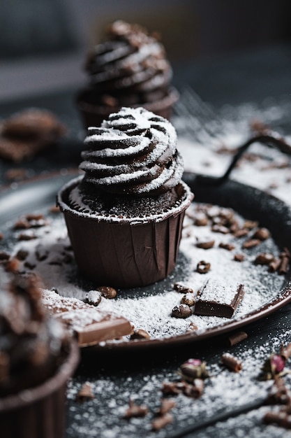 Several muffins or cupcakes with chocolate shaped cream at black table. Powdered sugar is scattered over the cakes.