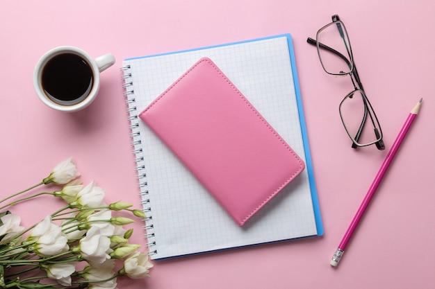 Several notebooks a cup of coffee and flowers on a bright pink background. top view. office tools