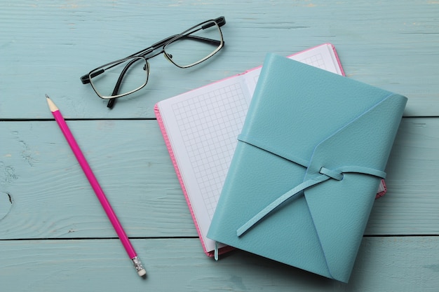 Several notebooks and a pencil and glasses on a light blue wooden table. top view. office tools