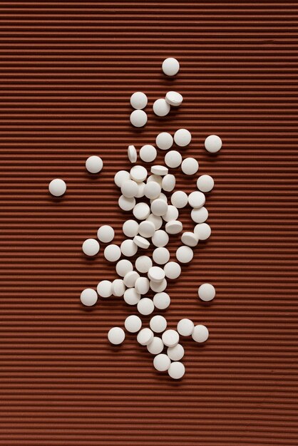 Several small white round tablets are randomly distributed across on brown textured background