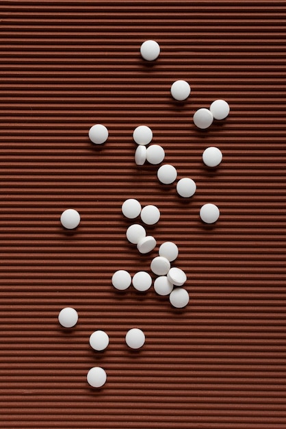 Several small white round tablets are randomly distributed across on brown textured background