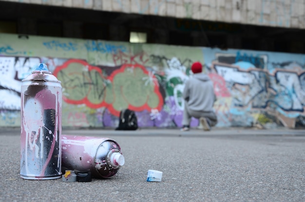 Several used spray cans with pink and white paint lie on the asphalt against the standing guy