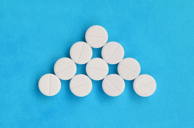 Several white tablets lie on bright blue in the form of a triangular arrow.