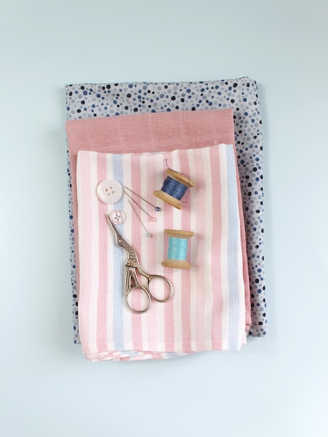 Sewing accessories and fabric on a blue background Sewing threads needles pins fabric buttons and sewing centimeter top view flatlay