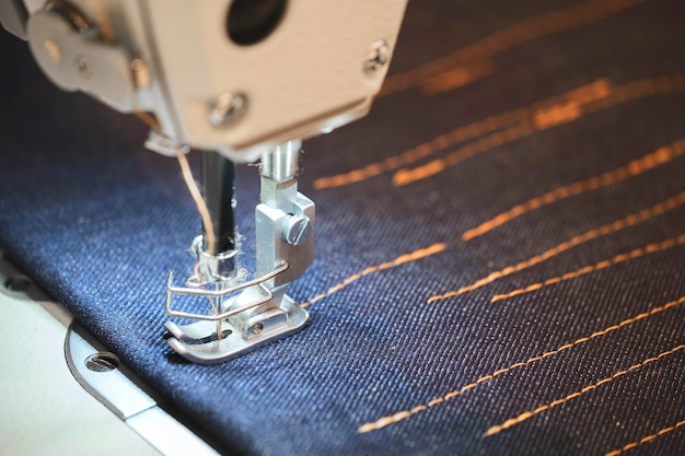 Photo sewing machine sews blue denim with orange threads closeup