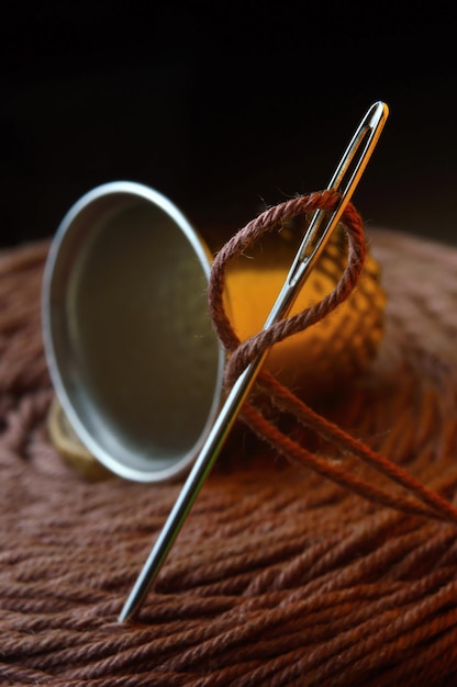 Sewing needle with thread inserted into it. against the background of a large bobbin of thread and a thimble. close-up.