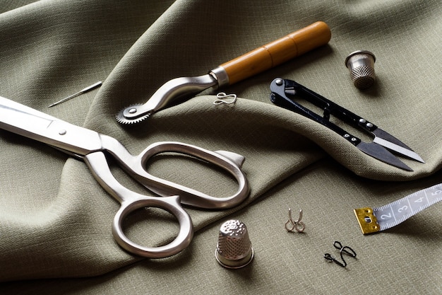 Sewing supplies lie on draped fabric, close-up. Sewing background. Spools of thread, a centimeter, scissors, a thimble, on a gray draped cloth. Atelier concept. Fashion designer. Sewing composition.