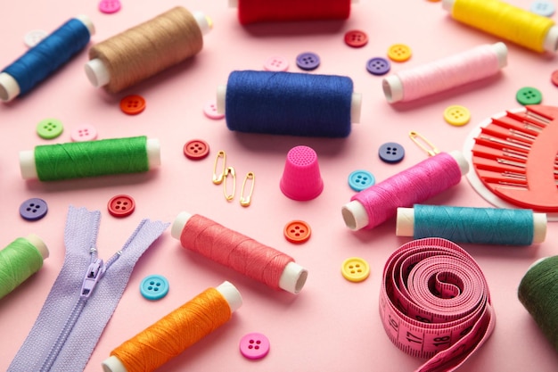 Sewing supplies on pink background sewing thread scissors a large spool of thread pieces of cloth needlescentimeter buttons