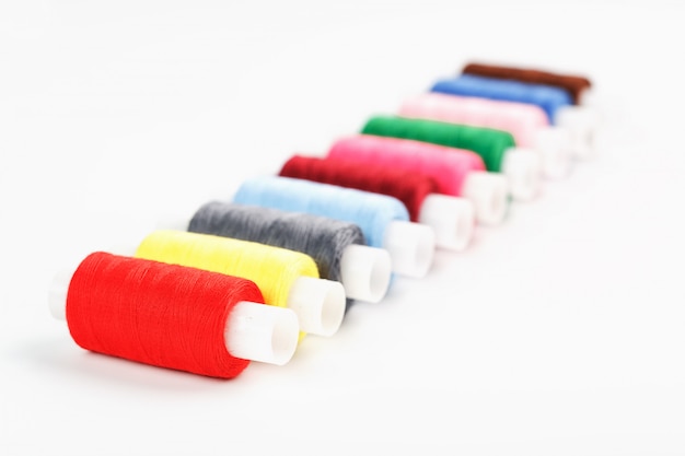 Sewing threads of different colors on reels on white.