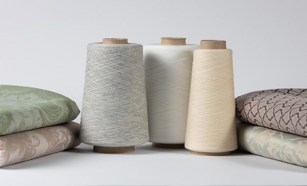 Sewing threads on wooden spools with bed linen on white isolated background