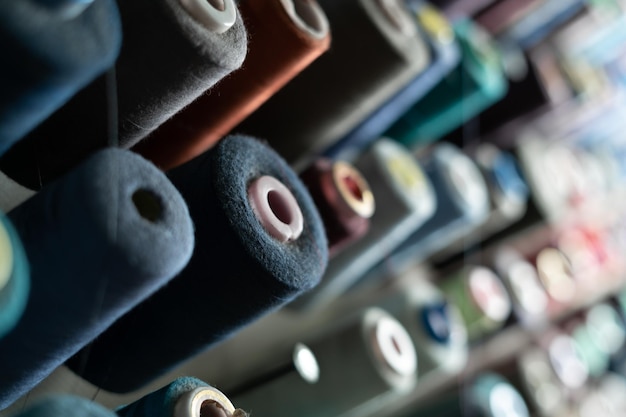 In a sewing workshop many spools of thread of different colors hang on a metal wall Tailoring concept and variety of materials