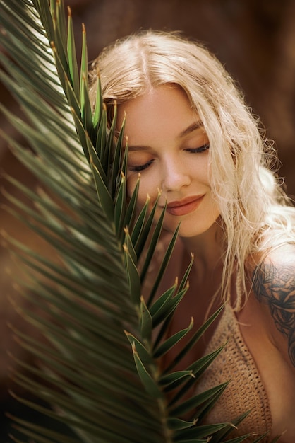 Sexy beach blonde girl in knitted bikini with palm leaf outdoors on nature