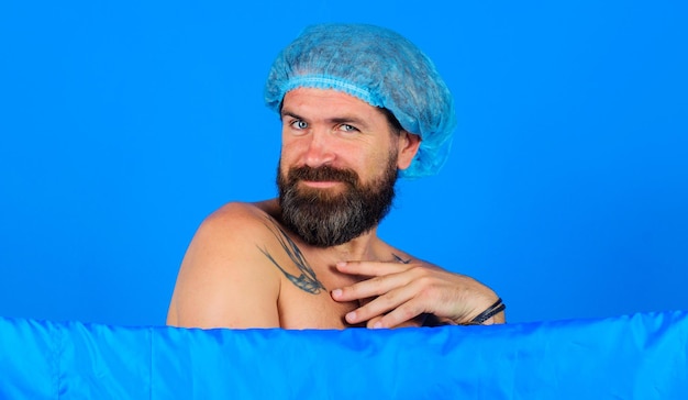 Sexy bearded man in in bathing cap taking shower body washing