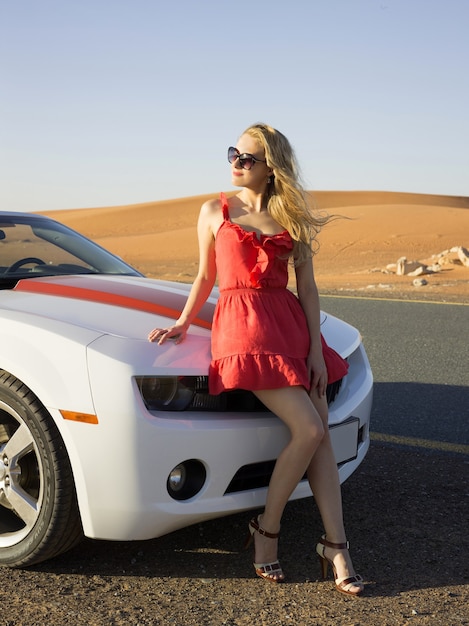 Sexy blond girl sit on convertible car hood at desert