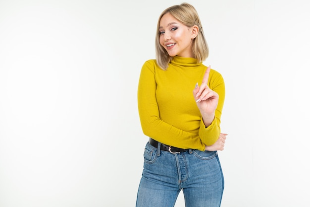 Sexy blonde young woman in tight lemon blouse and jeans threatens with index finger on a white background