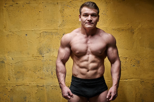 Photo sexy bodybuilder man posing on yellow background in black shorts. handsome pumped male body isolated with free space for advertising