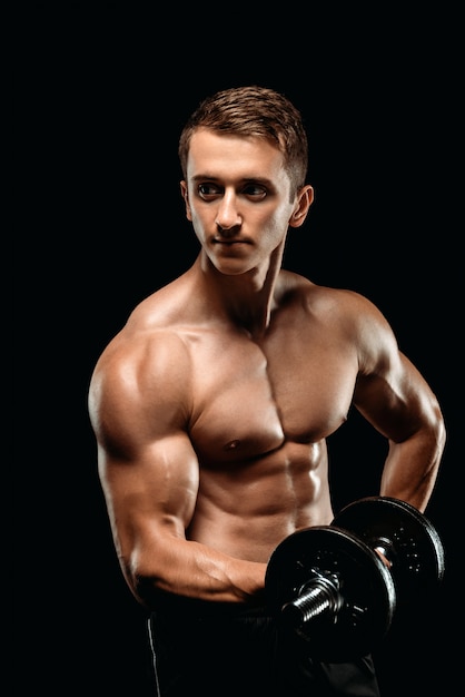 Sexy bodybuilder with muscular torso exercising with dumbbell isolated on black