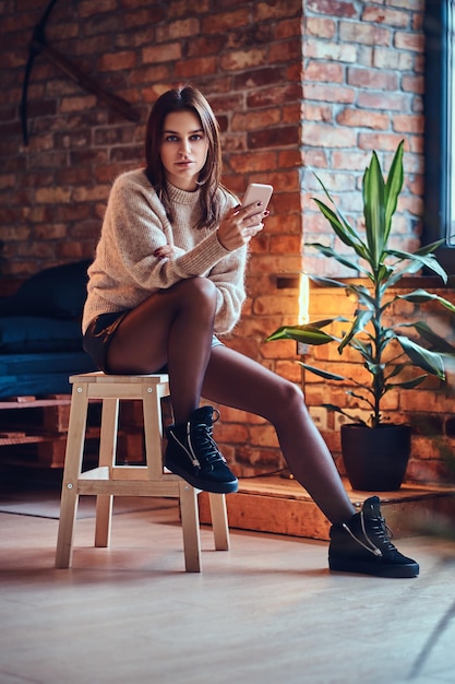 Sexy brunette female using a smart phone in a room with loft interior.