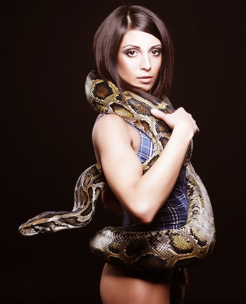 Sexy brunette holding python over black wall