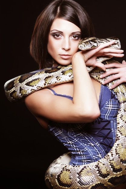 Sexy brunette holding python over black