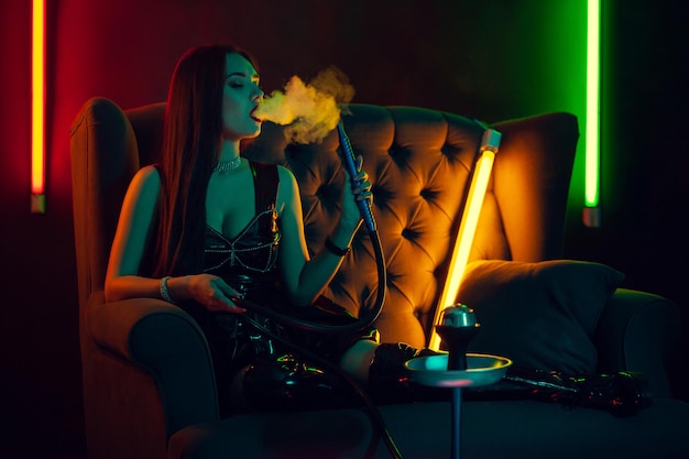 Sexy brunette model is smoking a hookah exhaling a smoke at a luxury night club.