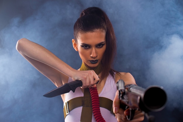 Sexy brunette in a white t-shirt with a gun in his hands. Against the background of smoke