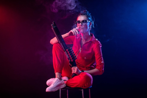 Sexy bully girl smokes a cigarette with a shotgun on a dark background in neon light and a haze of copy paste